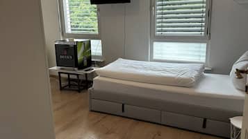 Une chambre à coucher avec un lit, un téléviseur fixé au mur et une fenêtre avec des stores.