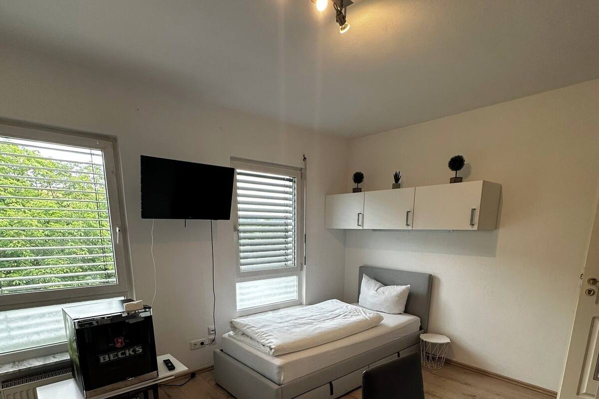 Ein Schlafzimmer mit einem Bett, einem Schreibtisch mit Fernseher, einem Fenster und einem Schrank.
