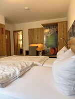 Quarto de hotel com duas camas, painéis de madeira, um mural com vista para montanhas e uma pequena mesa com abajur.