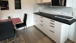 A modern kitchen with white cabinets, a black countertop, a microwave, and a dining area with a table and chairs. - Hotel-Restaurant Dechbettener Hof (Regensburg)