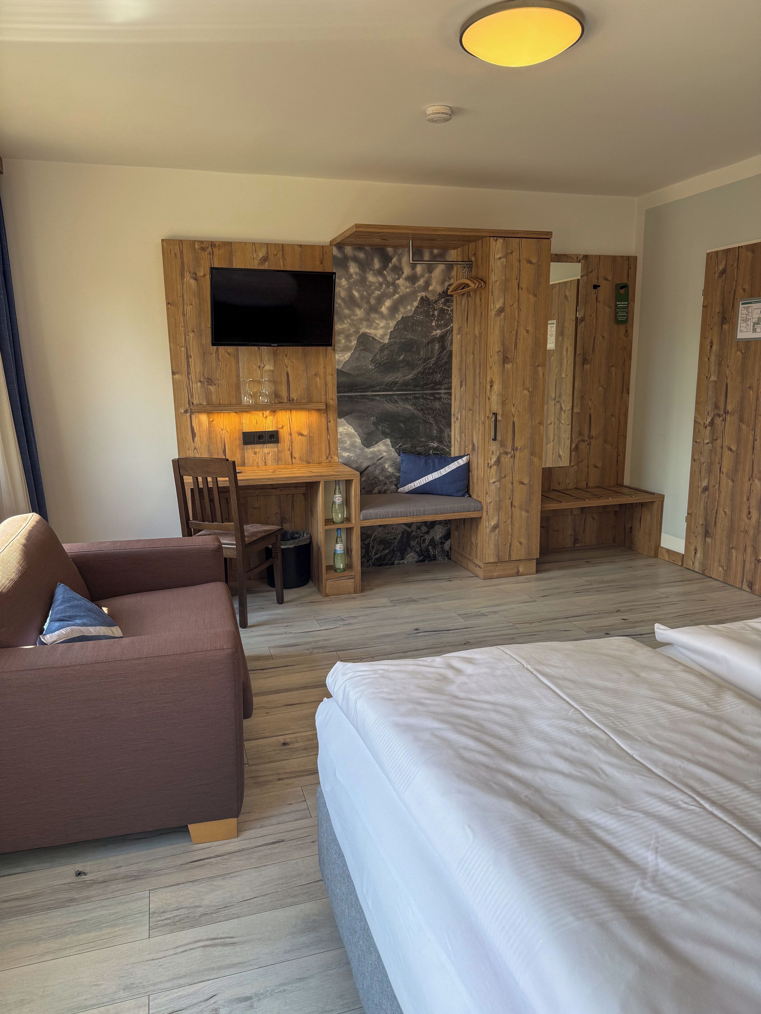 A room with a bed, a sofa, a desk with a TV, and a wooden wardrobe.