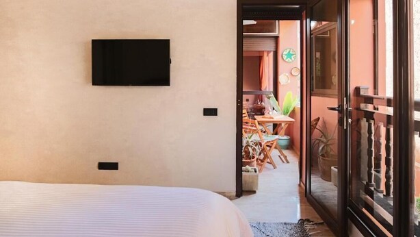 Un dormitorio con cama, televisor montado en la pared y puerta corrediza de vidrio que da a un balcón con plantas.