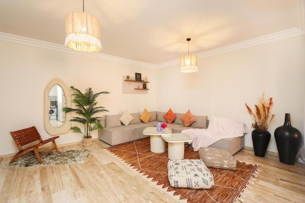 A living room with a sofa, coffee table, and a chair. There is a mirror, a potted plant, and a vase with dried flowers.