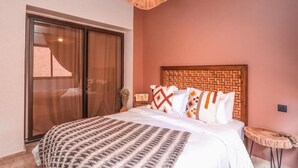 Un dormitorio con cama, cabecera de madera, una mesita redonda y una puerta corrediza de vidrio.