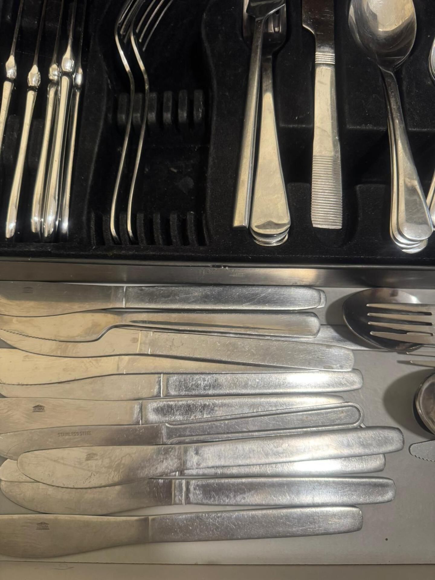 A set of stainless steel cutlery including forks, knives, and spoons, neatly arranged in a compartment.