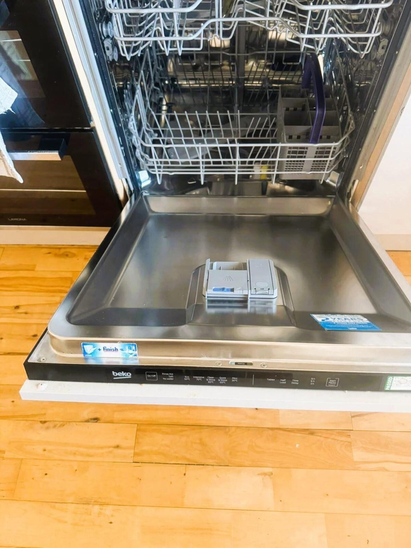 Un lave-vaisselle ouvert, avec un panneau de commande et un autocollant bleu sur la porte.