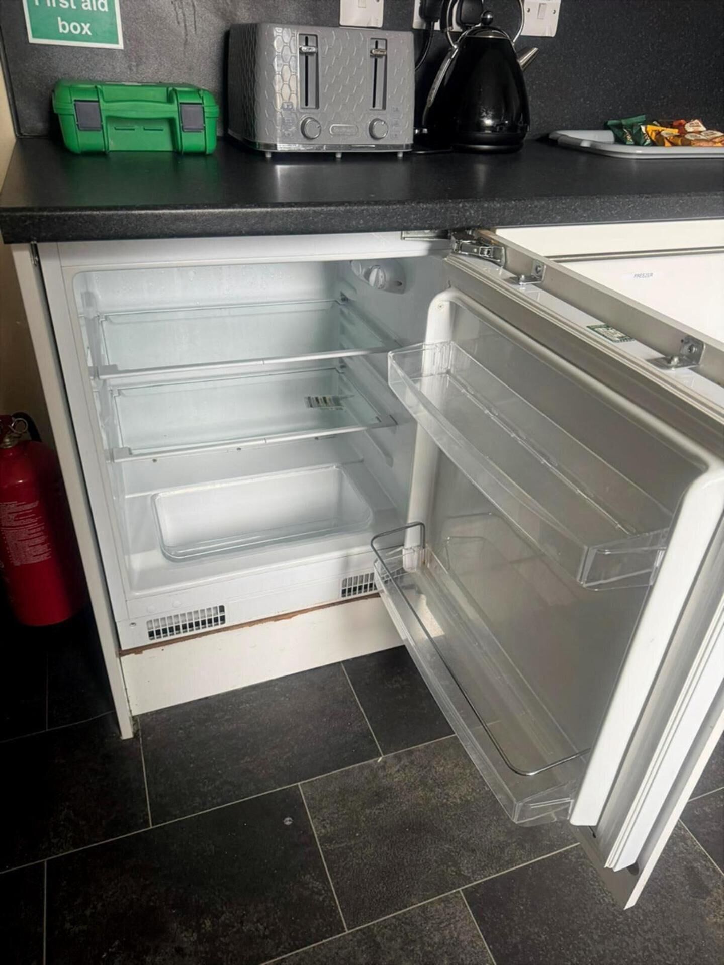 Un refrigerador abierto con repisas transparentes, una tetera y un tostador en la encimera.
