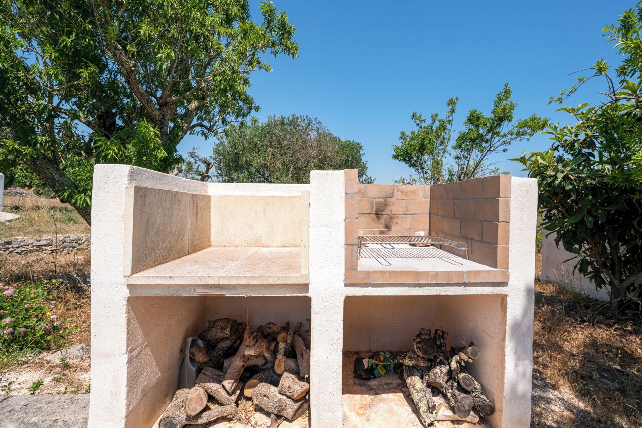 A stone barbecue grill with a metal grate, surrounded by a low stone wall.