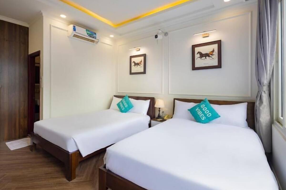 Een hotelkamer met twee bedden, houten vloeren, wit beddengoed en een plafond met inbouwspots.