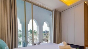 Habitació d'hotel amb un llit gran, vista per finestres del terra al sostre i un balcó amb mobles d'exterior.