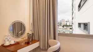 Habitació d'hotel amb escriptori de fusta, una cadira, un mirall, una ampolla de xampany i vista a la ciutat.