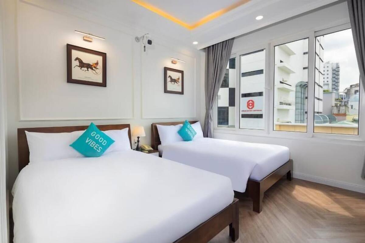 Een hotelkamer met twee bedden, uitzicht op de stad en kunstwerken in lijsten aan de muren.