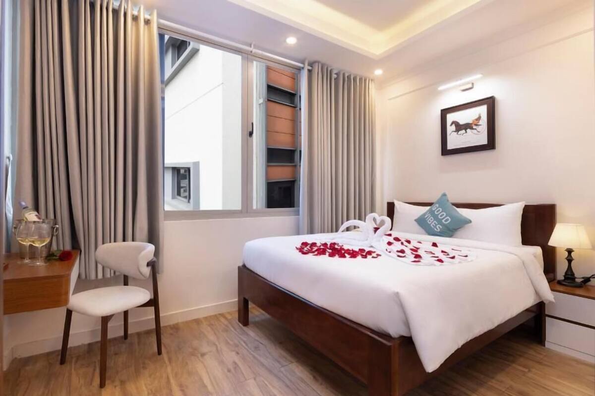 Een hotelkamer met een bed, een stoel, een nachtkastje met lamp, een schilderij aan de muur en een raam met gordijnen.