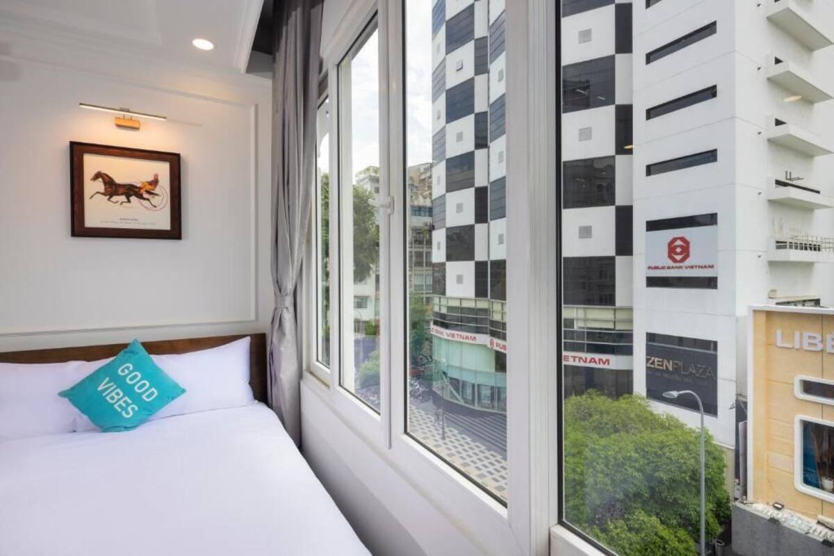Hotelkamer met een bed, een ingelijst schilderij aan de muur en een raam met uitzicht op een gebouw.