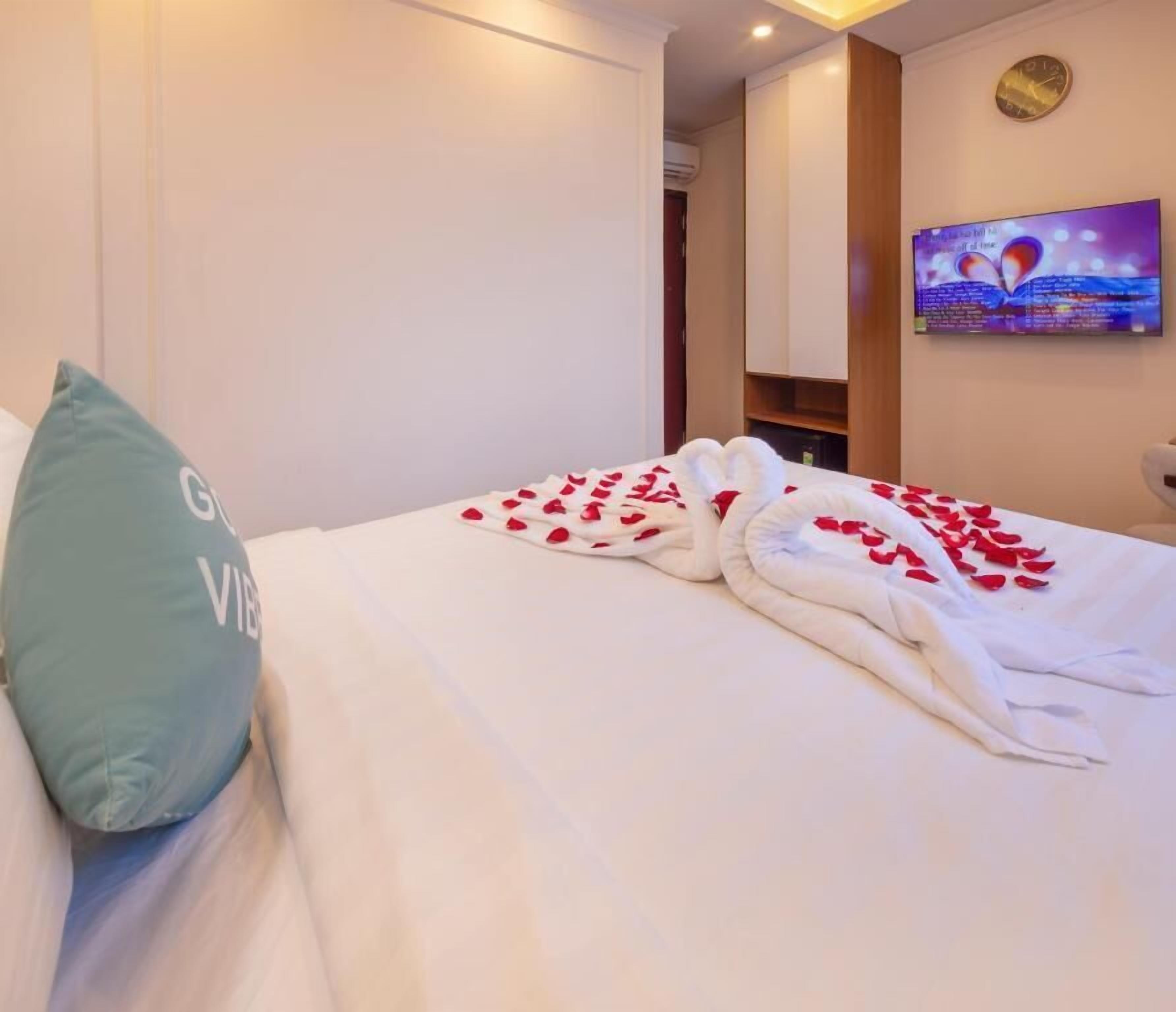 A hotel room with a bed, a teal pillow, and a wall-mounted TV displaying a scenic view.
