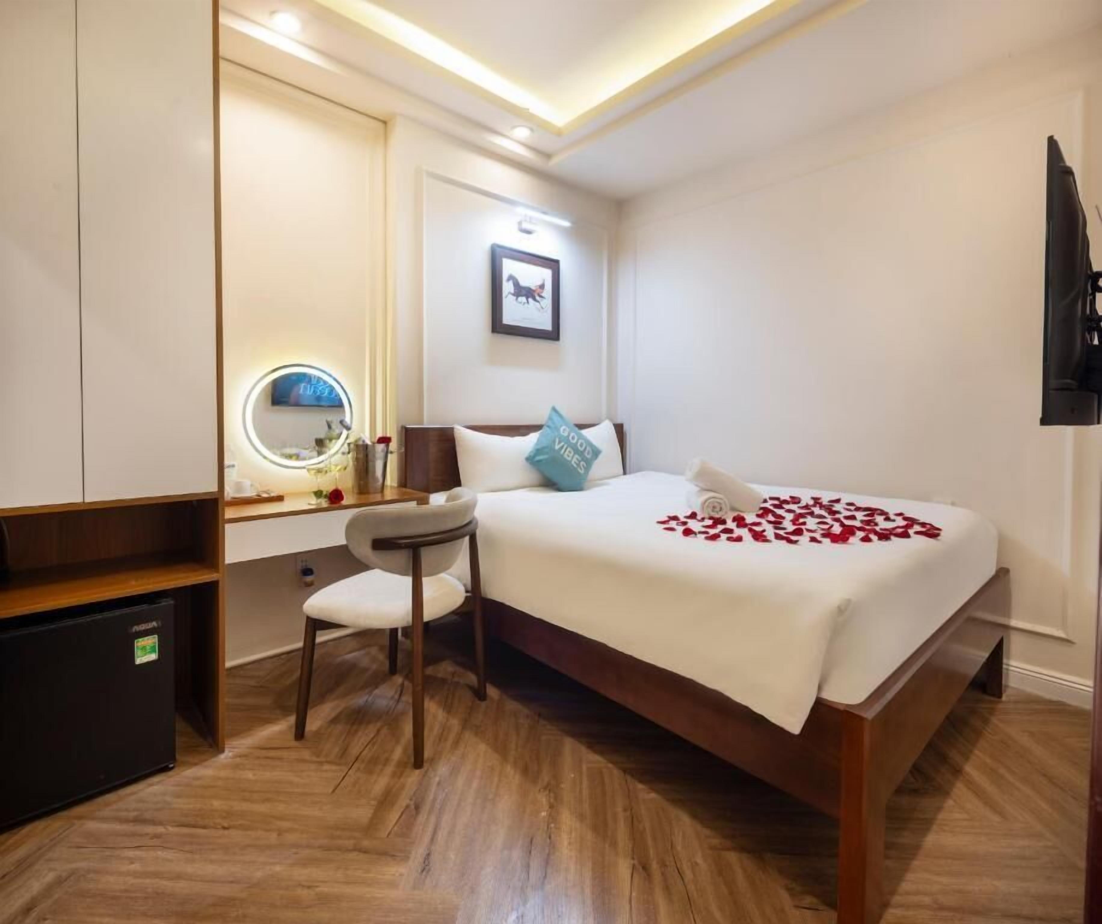 A hotel room with a bed, bedside table, chair, and a small desk with a mirror.