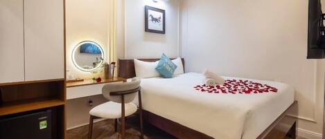 A hotel room with a bed, bedside table, chair, and a small desk with a mirror.