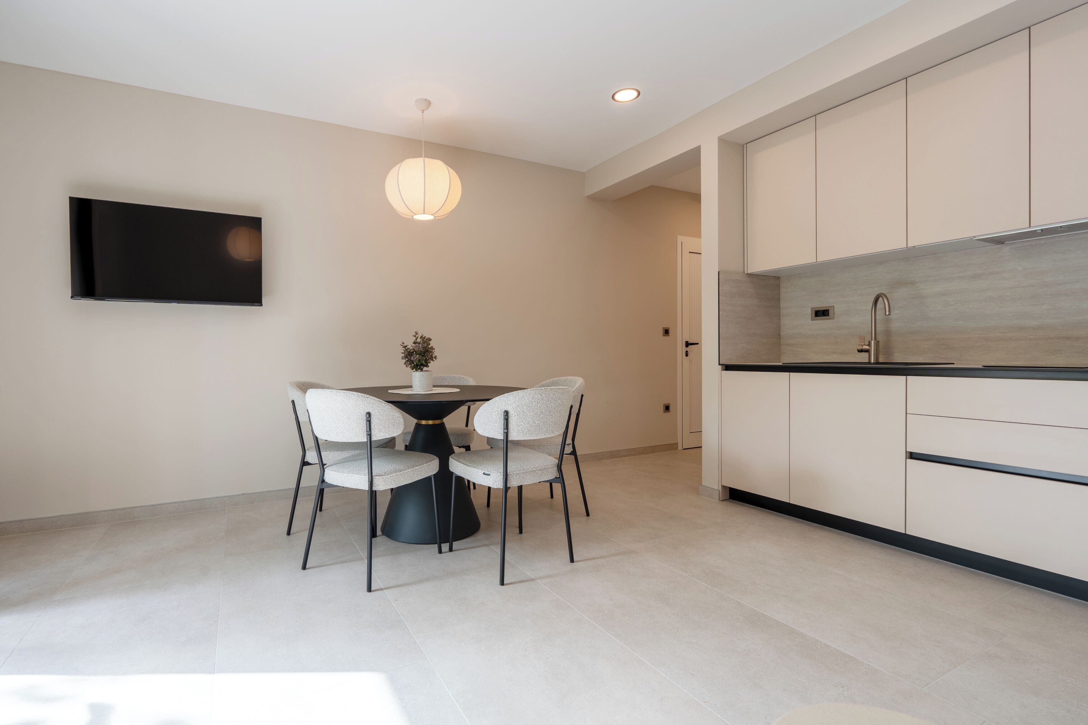 Een moderne keuken met witte kasten, een zwart aanrecht en een eethoek met een ronde tafel en vier stoelen.