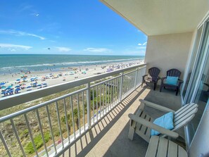 Ein Balkon mit Blick auf einen Strand, Stühlen und einem Geländer.