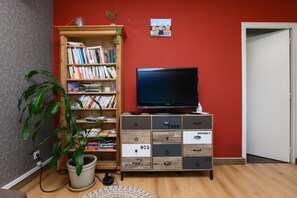 A room with a bookshelf, a television, a potted plant, and a door. - Apartment 'Sarzeau City Center on Foot' with Wi-Fi and Air Conditioning (Sarzeau)