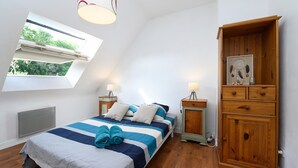 A bedroom with a skylight, a bed with striped bedding, bedside tables with lamps, and a wooden cabinet. - Apartment 'Sarzeau City Center on Foot' with Wi-Fi and Air Conditioning (Sarzeau)
