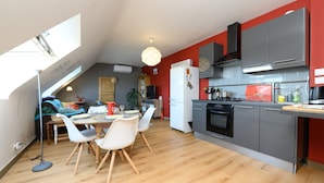 A modern kitchen with grey cabinets, a white refrigerator, and a dining area with a wooden table and white chairs. - Apartment 'Sarzeau City Center on Foot' with Wi-Fi and Air Conditioning (Sarzeau)