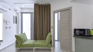 Una sala moderna con un sofá verde, una zona de cocina con microondas y una puerta que da a otra habitación.