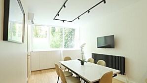Ett modernt matrum med ett stort bord, stolar, en orkidé i en kruka, en tv och ett element.