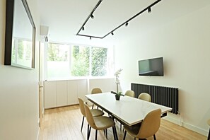 Ein stilvoller Essbereich mit einem großen Tisch, Stühlen, einer Topf-Orchidee, einem Fernseher und einer Heizung.