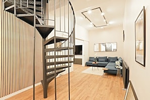 Ein modernes Wohnzimmer mit einer Wendeltreppe, einem Sofa, einem Couchtisch und einem Flachbildfernseher.