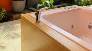 Una vasca da bagno in legno con rubinetteria cromata, circondata da piante in vaso e una parete in pietra.