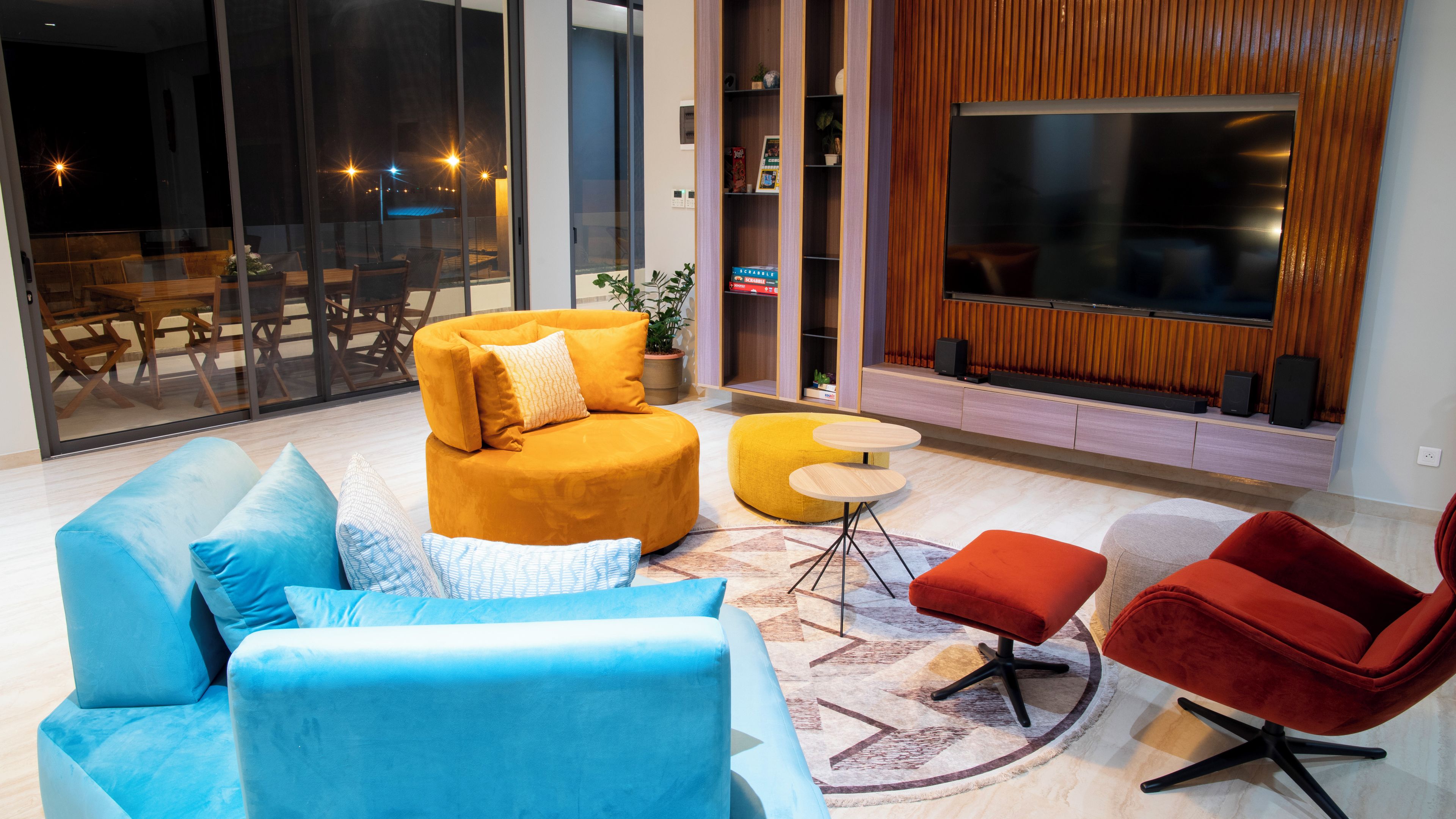 A modern living room with a sofa, ottoman, and chairs, a television, and a bookshelf.