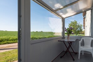 Ein Zimmer mit großem Fenster, kleinem Tisch, einer Vase und einem weißen Stuhl.