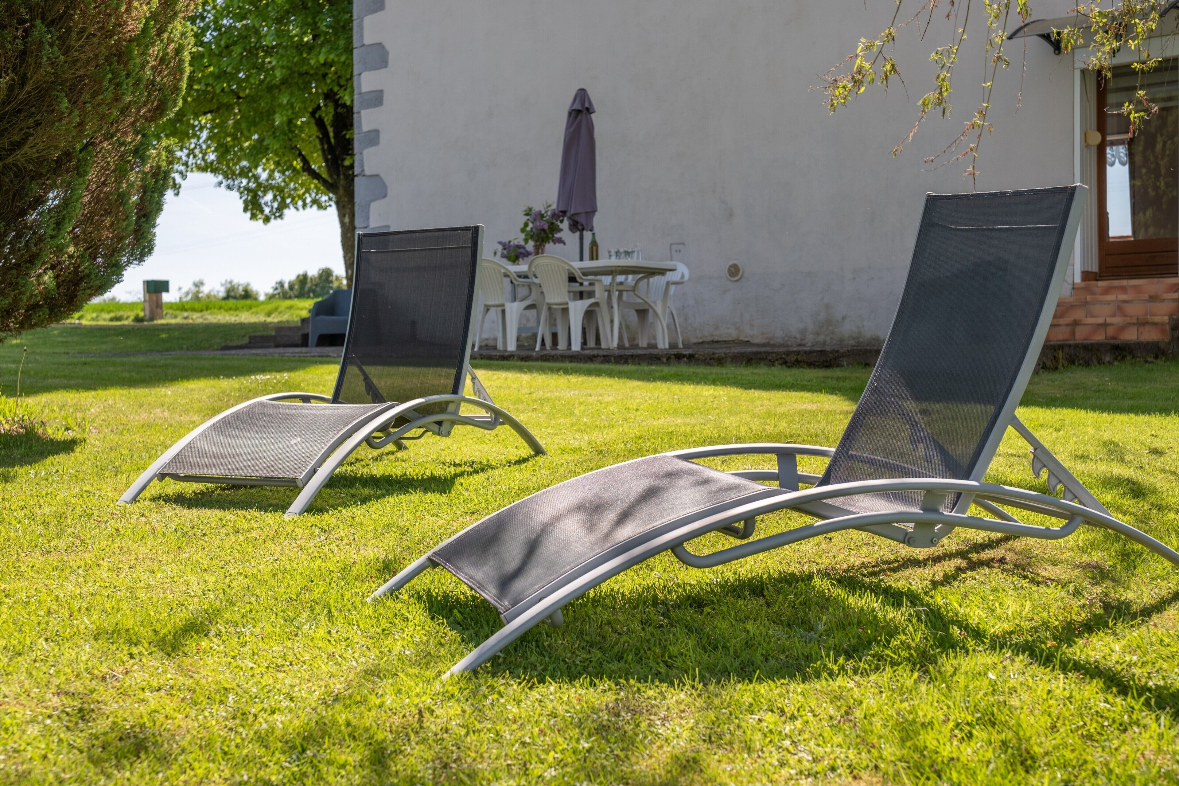 Dos sillones reclinables con estructura de metal y respaldo de malla, ubicados sobre un césped.