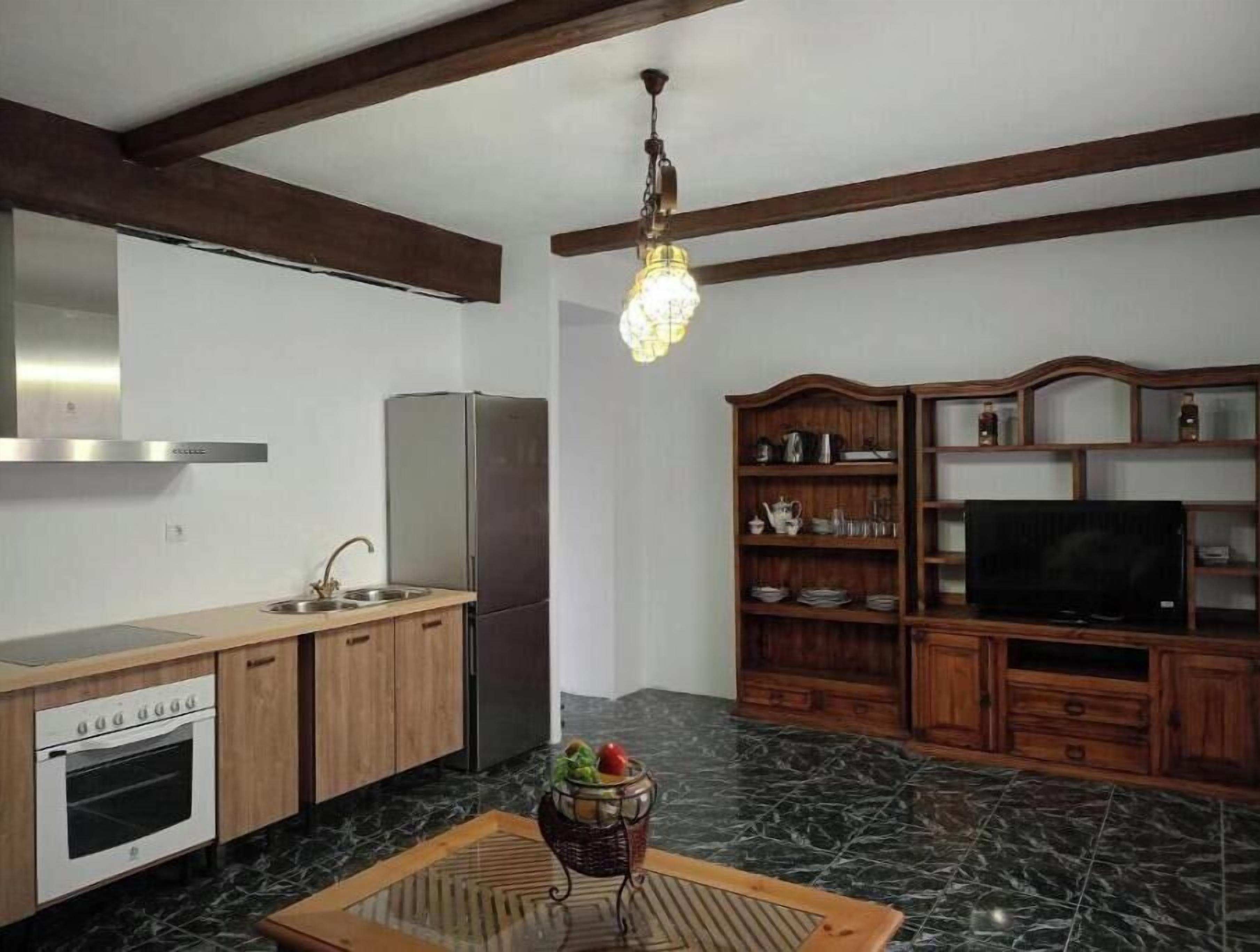 Eine Küche mit Kühlschrank, Backofen und Spüle; ein Essbereich mit Tisch und Stühlen; ein Fernseher auf einem Holzschrank; und eine Kristallleuchter.