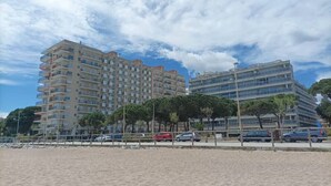 A beachfront hotel with multiple floors, a sandy beach in the foreground, and a clear sky. - Luminous apartment with two balconies and swimming pool in front of the sea (Blanes)