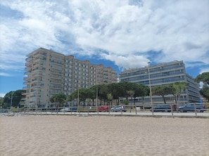 Ein Hotel direkt am Strand mit mehreren Etagen, ein sandiger Strand im Vordergrund und ein klarer Himmel.