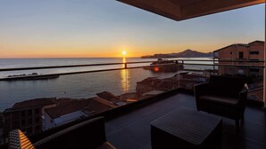 Un balcon offrant une vue sur le coucher de soleil sur la mer, un pont et un paysage montagneux.