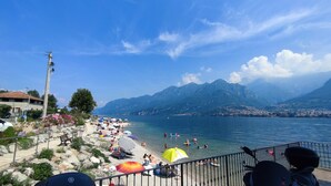 A beach with people, umbrellas, and mountains in the background. - Little Gem Challet - Trekking House Como Lake (Torno)