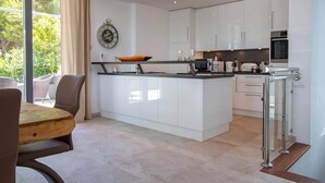 Een moderne keuken met witte kasten, een centraal eiland en een eethoek met een houten tafel en stoelen.