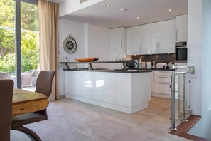A modern kitchen with white cabinetry, a central island, and a dining area with a wooden table and chairs. - Exclusive Villa in the Southwest of Mallorca (Santa Ponsa)