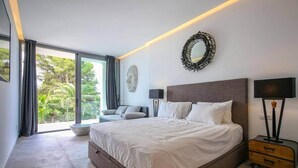 Een moderne slaapkamer met een groot bed, een bank, een ronde spiegel en een nachtkastje.