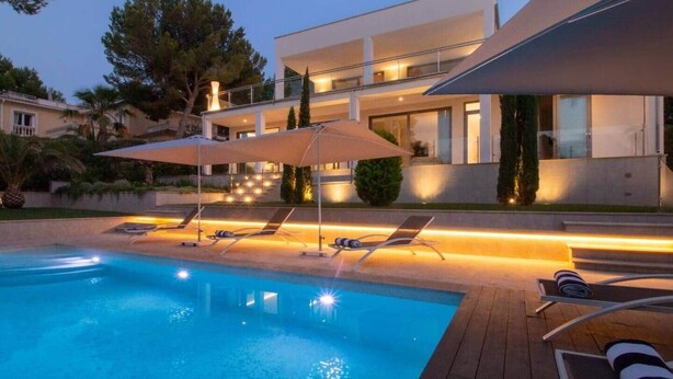Een modern huis met een zwembad, ligbedden en een overdekt terras.