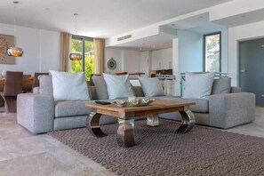 A modern living room with grey sofas, a wooden coffee table, and a large window. - Exclusive Villa in the Southwest of Mallorca (Santa Ponsa)