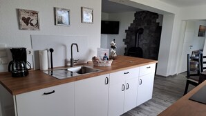 A modern kitchen with a wooden countertop, white cabinets, a coffee maker, and a stone fireplace. - Seagull's nest in the middle of the countryside (Dornum)