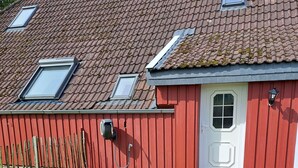 A red building with a white door, a small window, and a skylight. - Seagull's nest in the middle of the countryside (Dornum)