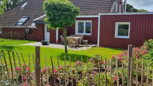 A red building with a garden, a wooden fence, and a table with chairs. - Seagull's nest in the middle of the countryside (Dornum)
