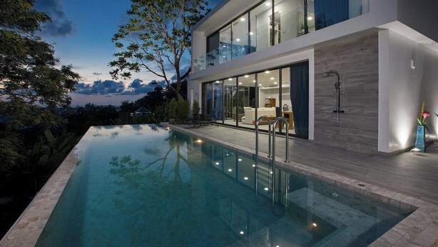 Ein modernes Haus mit Schwimmbad, großen Fenstern und einem Balkon.