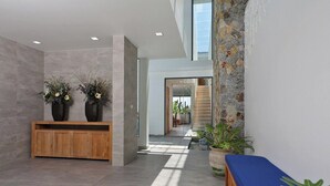 Eine moderne Lobby mit einem hölzernen Empfangstresen, zwei großen Vasen mit Blumen, einer blauen Bank und einer Steinwand.