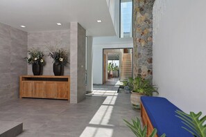 A modern lobby with a wooden reception desk, two large vases with flowers, a blue bench, and a stone wall. - Sugar | Kamala Beach | 4-bedroom Pool Villa (Kamala)